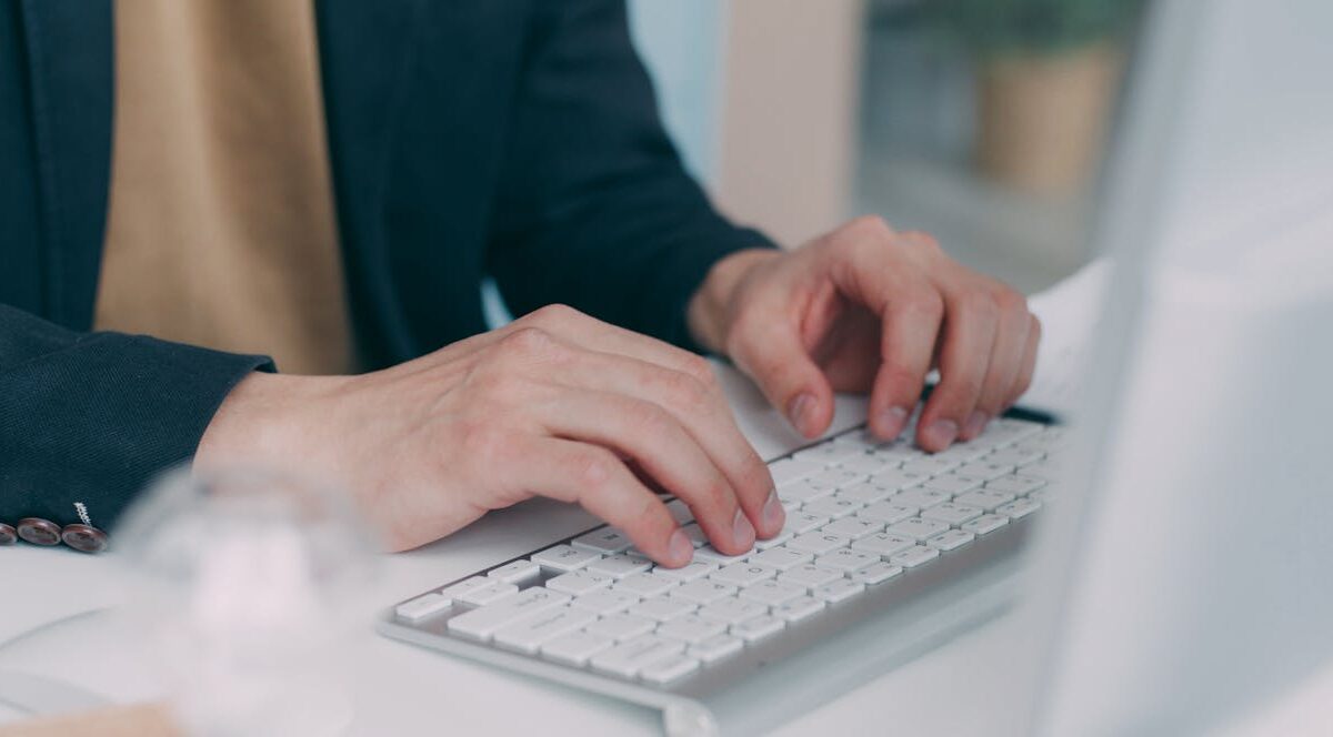 Close-up of hands typing on a computer keyboard in an office setting.